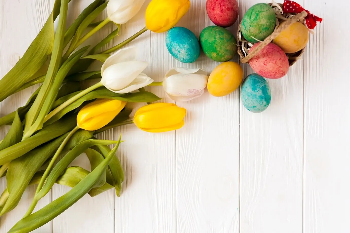 Тюльпаны рядом с пасхальными яйцами и небольшой корзиной.